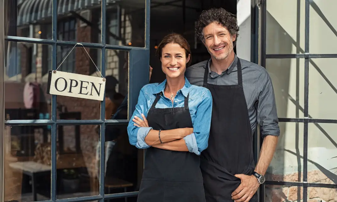 Local entrepreneurs stand proudly outside their startup, welcoming customers with an ‘OPEN’ sign.