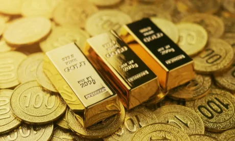 Shiny gold bars stacked atop a pile of embossed gold coins. Visual for a Guide to Gold Trading, highlighting purity, value, and the allure of precious metals.